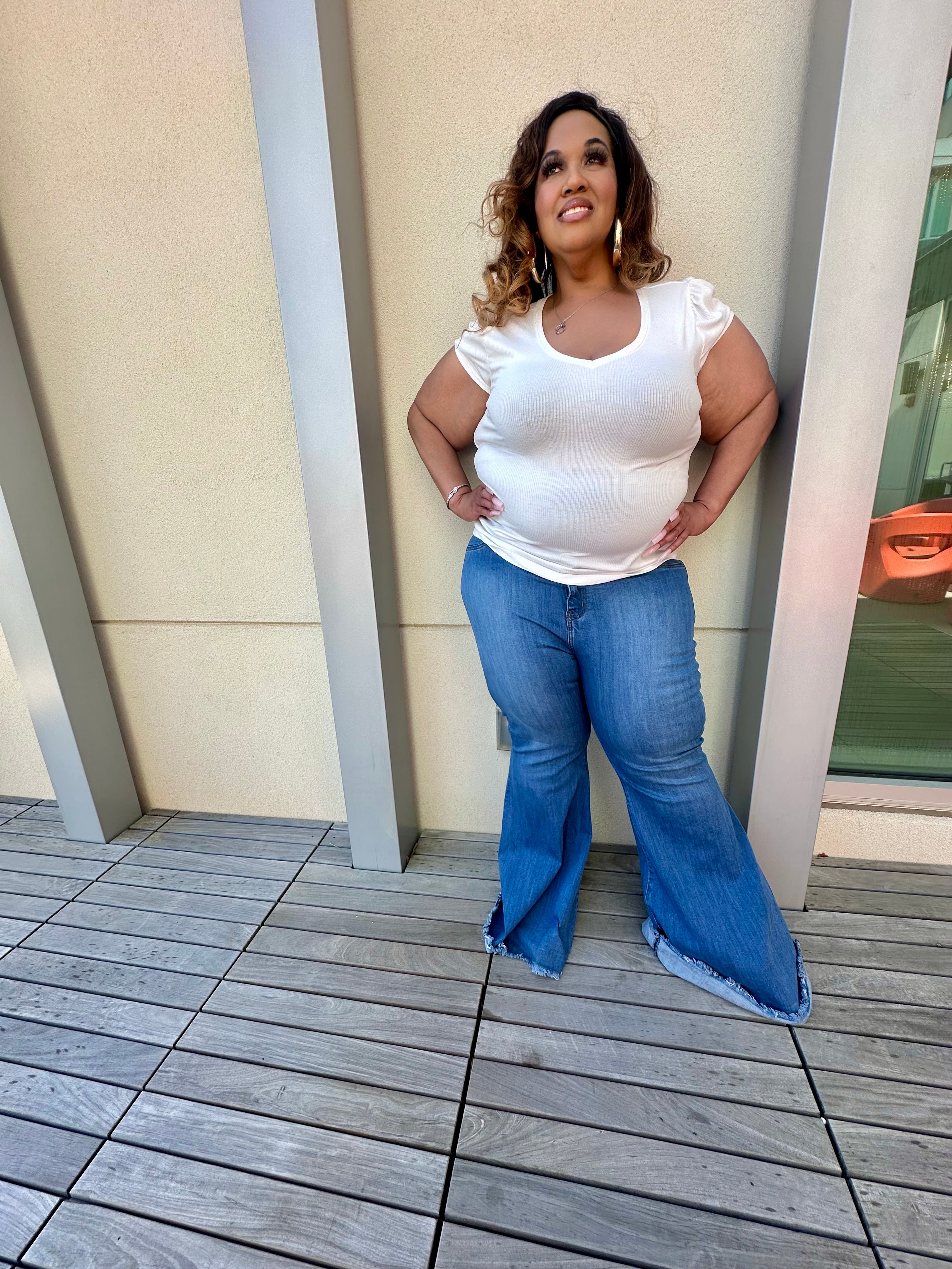Plus-size tall woman wearing best-fitting bell-bottom flare jeans in medium blue denim, styled for curves and height. Hands on hips