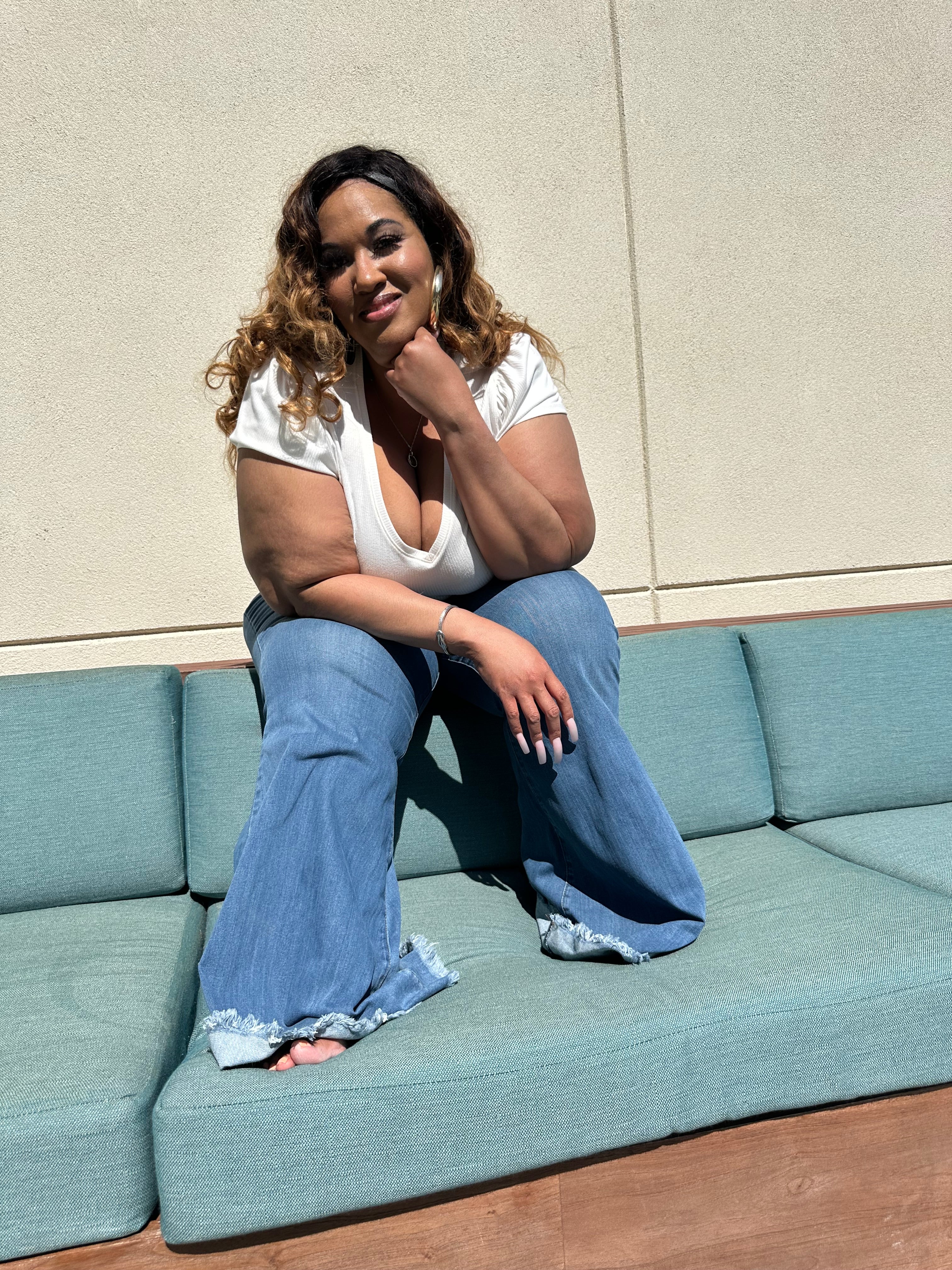 Plus-size tall woman wearing best-fitting bell-bottom flare jeans in medium blue denim, styled for curves and height, hand on chin sitting.