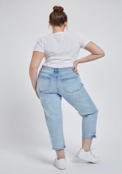 Plus-size model wearing light wash cropped mom jeans with distressed hem, ultra-high rise, and stretch fit for plus-size curves, back pocket.