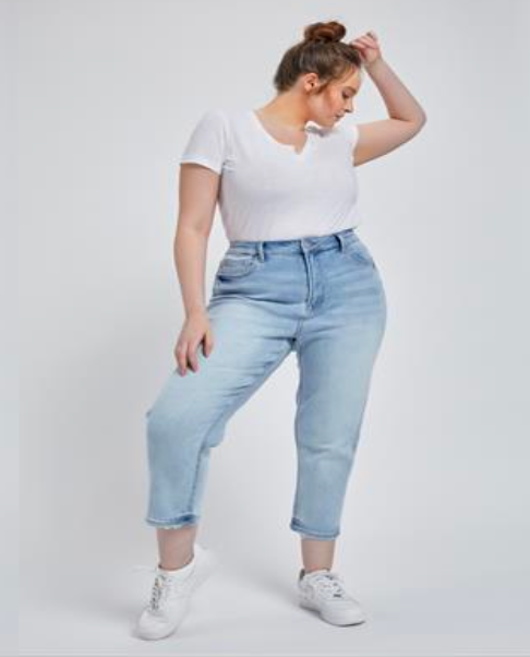 Plus-size model wearing light wash cropped mom jeans with distressed hem, ultra-high rise, and stretch fit for plus-size curves, tip toe.