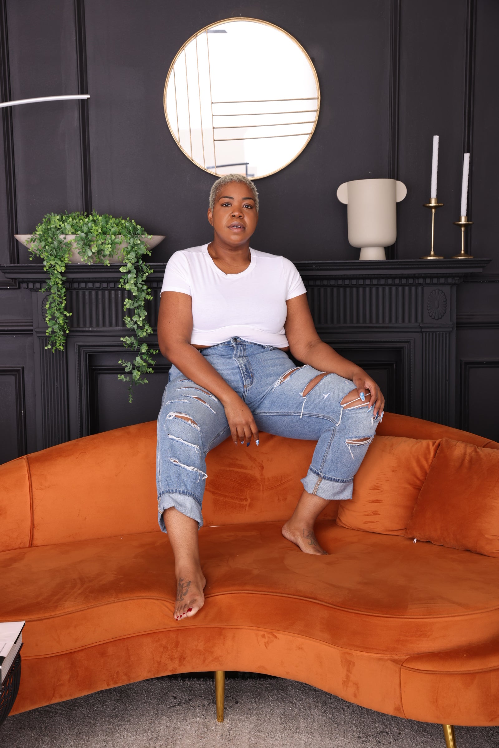 Plus-size woman in Raquel mid-rise rigid boyfriend jeans with front-leg distressed details, styled for a relaxed and structured fit. Couch